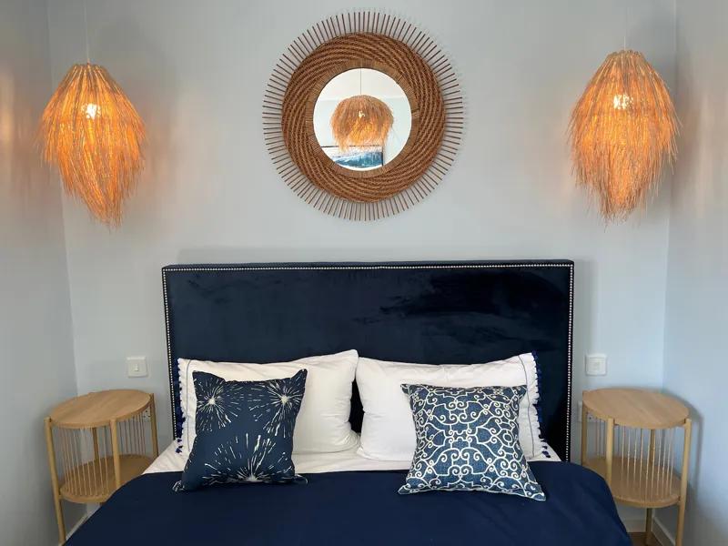 Double bedroom with navy bedding, a rattan mirror and two woven pendant lights